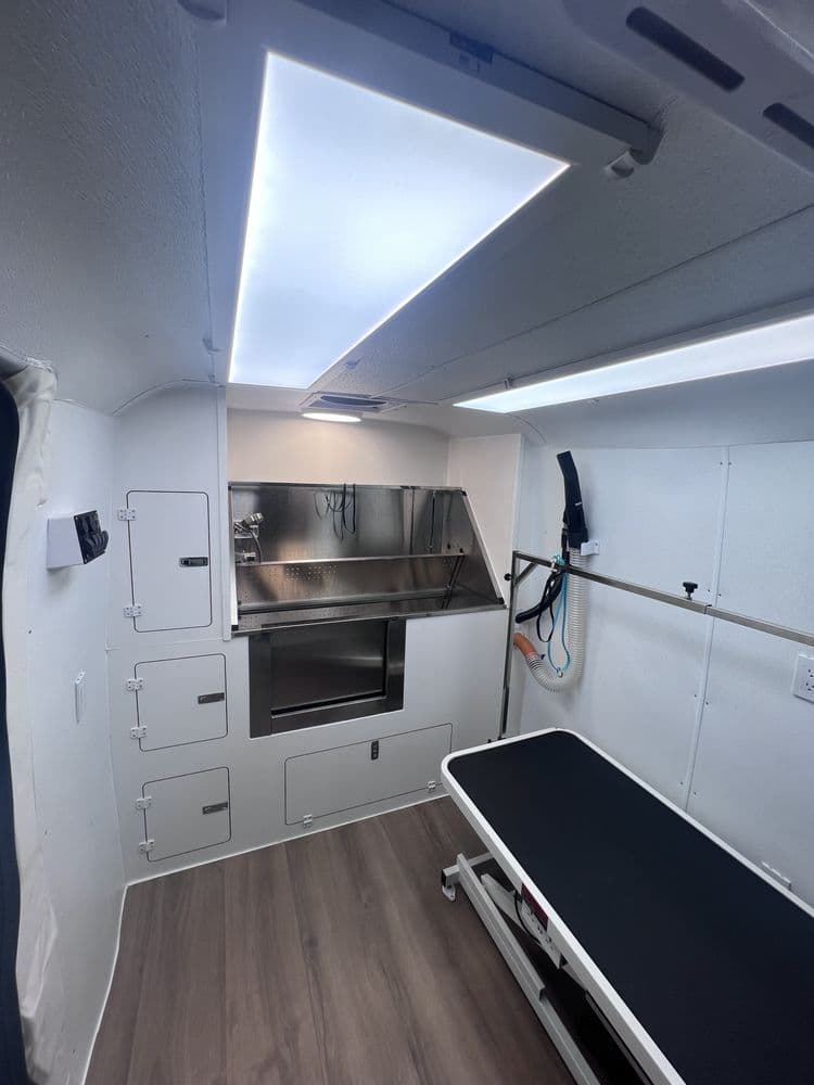 Inside the Bark and Bork mobile grooming van, showing the stainless steel tub, grooming table, and overhead lighting